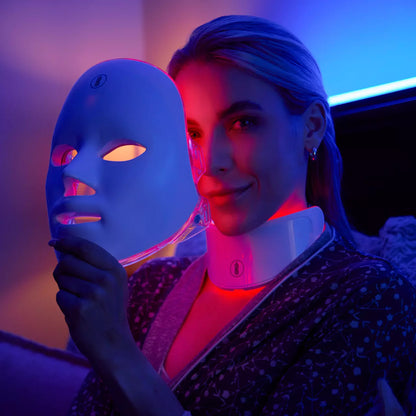 Woman holding a LED face mask with a blue and purple light in a dimly lit room.