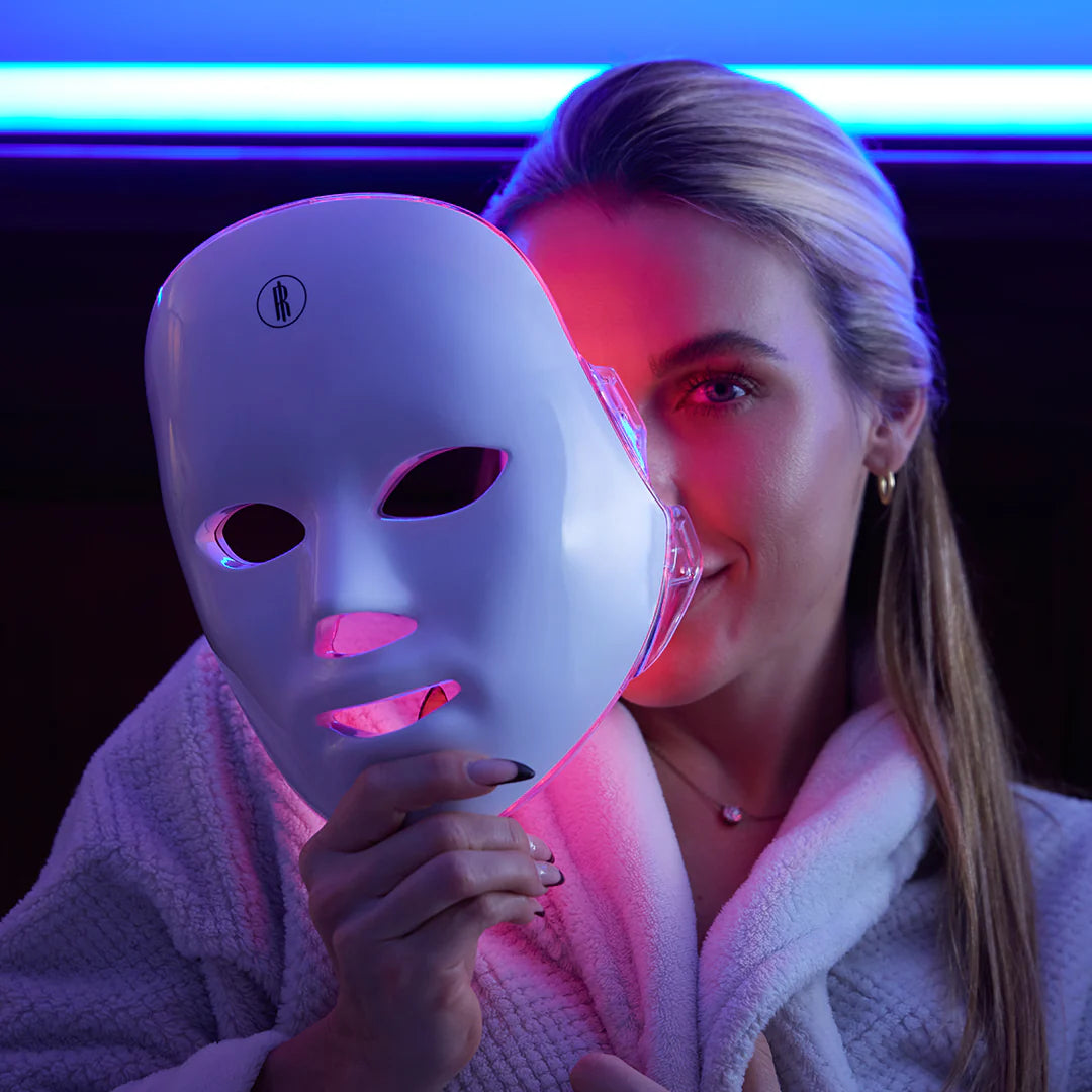 Woman holding a white LED face mask with colorful lighting in the background