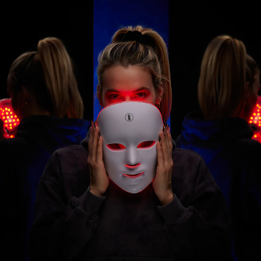 Person wearing a LED face mask with red lights in a dark setting